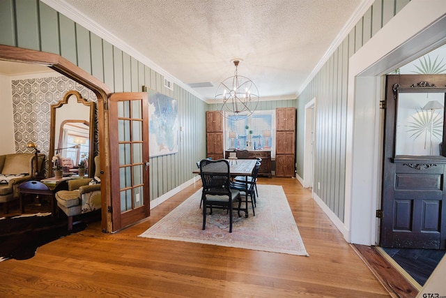 dining room with light wood finished floors, crown molding, arched walkways, a notable chandelier, and a textured ceiling