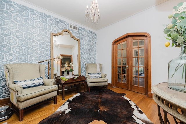 sitting room with wallpapered walls, wood finished floors, a chandelier, and ornamental molding