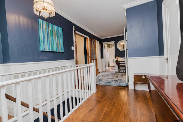 corridor with a notable chandelier, wainscoting, wood finished floors, and ornamental molding