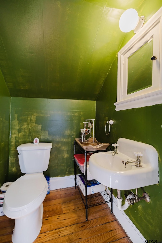 half bath with lofted ceiling, toilet, wood finished floors, and baseboards