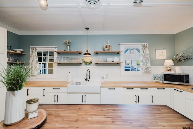 kitchen with stainless steel microwave, visible vents, open shelves, butcher block counters, and a sink