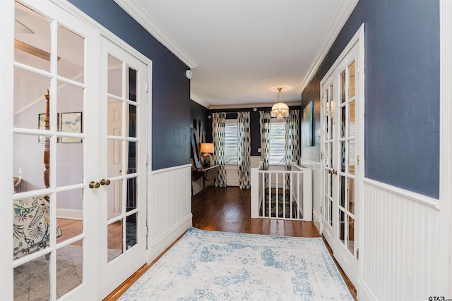 corridor featuring wood finished floors, an inviting chandelier, french doors, wainscoting, and crown molding