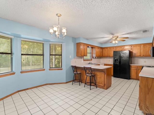 kitchen with ceiling fan with notable chandelier, kitchen peninsula, hanging light fixtures, a textured ceiling, and black refrigerator with ice dispenser