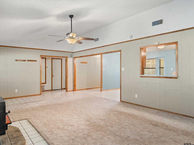 unfurnished room featuring a wood stove, a textured ceiling, wooden walls, light colored carpet, and ceiling fan