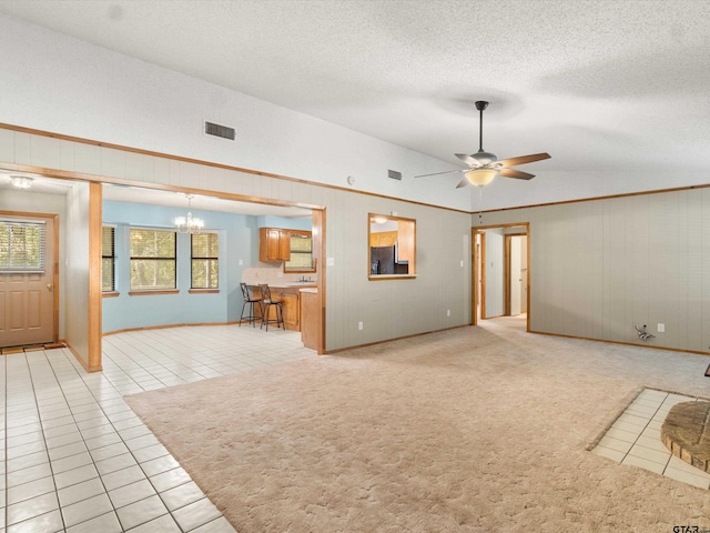 unfurnished living room with a textured ceiling, ceiling fan with notable chandelier, light tile patterned floors, and vaulted ceiling