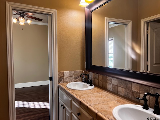 bathroom featuring wood-type flooring, decorative backsplash, vanity, ceiling fan, and crown molding