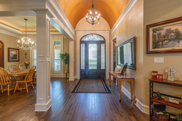 entrance foyer with dark hardwood / wood-style flooring, lofted ceiling, a notable chandelier, decorative columns, and ornamental molding