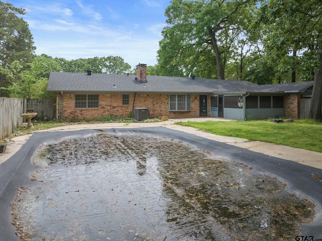 single story home featuring a chimney, a sunroom, brick siding, central AC, and fence