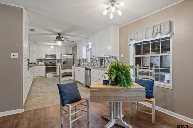 kitchen with light wood-style flooring, ceiling fan with notable chandelier, stainless steel appliances, white cabinetry, and tasteful backsplash