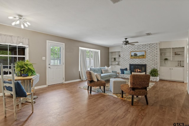 living room with a ceiling fan, built in features, a brick fireplace, wood finished floors, and baseboards