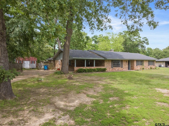 view of front facade featuring an outdoor structure, fence, a front yard, a storage unit, and brick siding