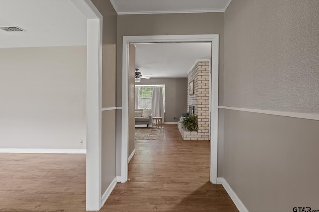 hallway featuring visible vents, ornamental molding, baseboards, and wood finished floors