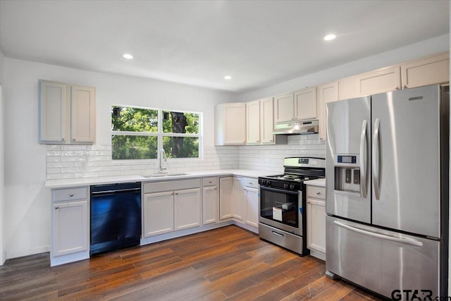 kitchen with a sink, backsplash, light countertops, under cabinet range hood, and appliances with stainless steel finishes