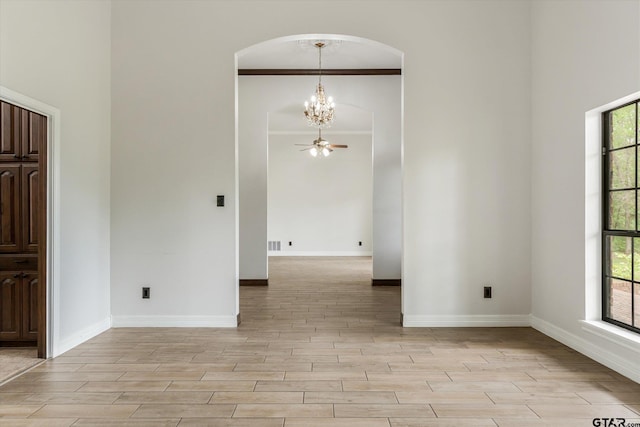 unfurnished room featuring light wood-type flooring, a wealth of natural light, and ceiling fan with notable chandelier