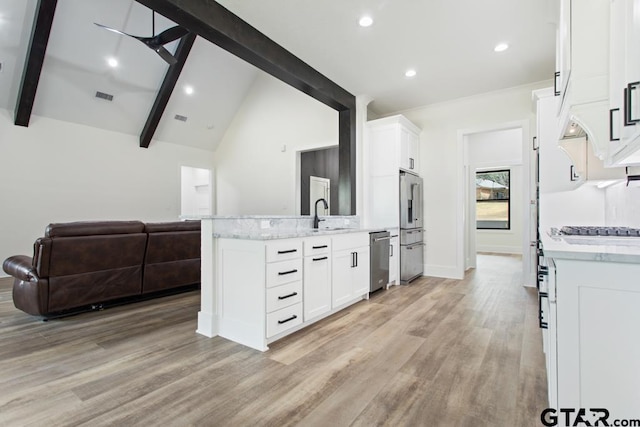 kitchen with white cabinets, appliances with stainless steel finishes, light wood-type flooring, and beamed ceiling