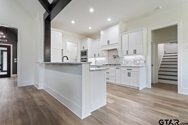 kitchen featuring tasteful backsplash, light hardwood / wood-style floors, lofted ceiling, white cabinets, and appliances with stainless steel finishes