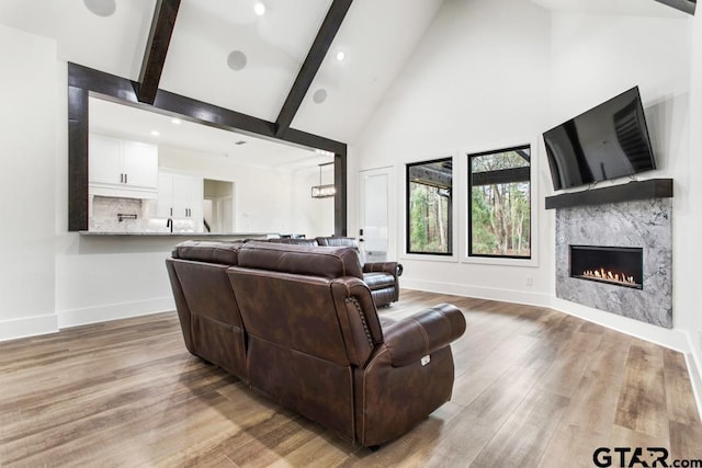 living room with a fireplace, high vaulted ceiling, light hardwood / wood-style floors, and beamed ceiling