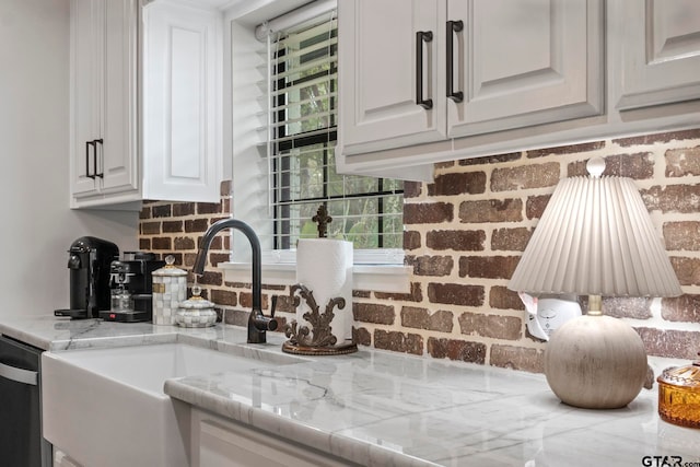 kitchen with sink, white cabinetry, stainless steel dishwasher, and brick wall