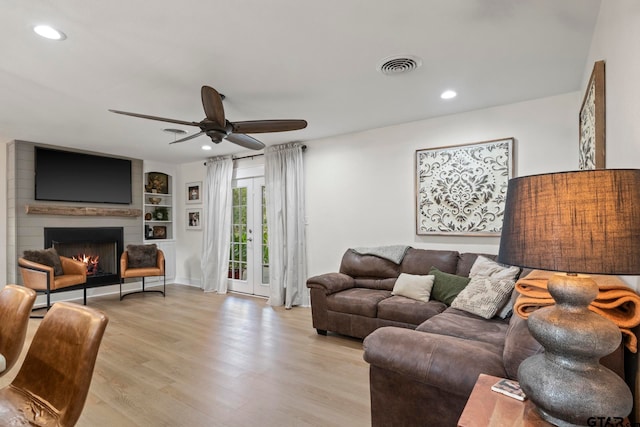 living room with built in shelves, a large fireplace, light hardwood / wood-style floors, and ceiling fan