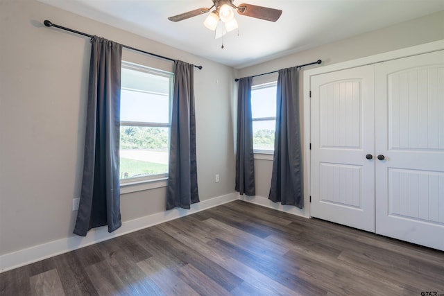 unfurnished bedroom with dark wood-type flooring, multiple windows, ceiling fan, and a closet