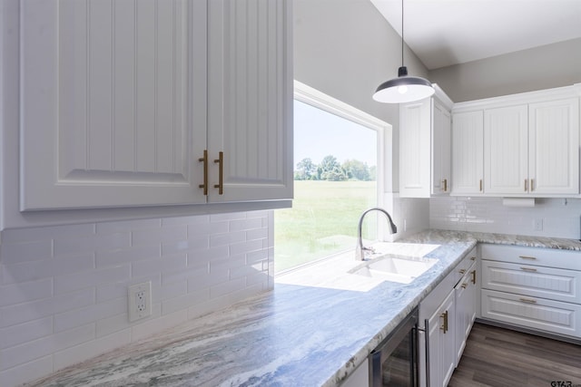 kitchen with tasteful backsplash, light stone counters, pendant lighting, sink, and white cabinets