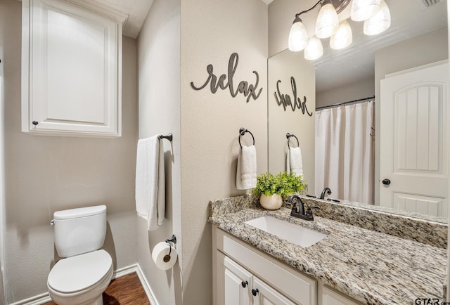 bathroom with vanity, wood finished floors, baseboards, toilet, and a textured wall