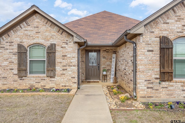 entrance to property with brick siding and a shingled roof