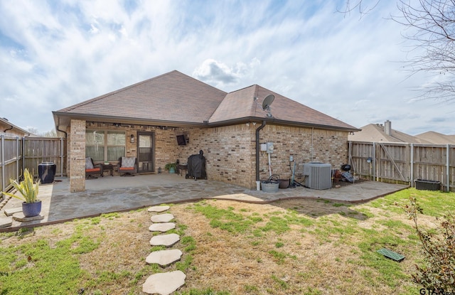 rear view of property featuring a patio, central AC, a fenced backyard, a yard, and brick siding