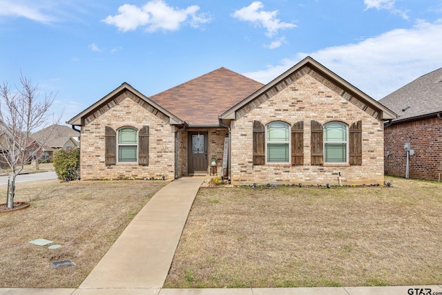 french provincial home with brick siding, a front yard, and roof with shingles