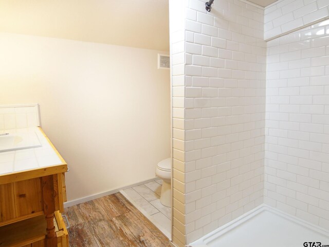 bathroom featuring visible vents, toilet, vanity, and tiled shower