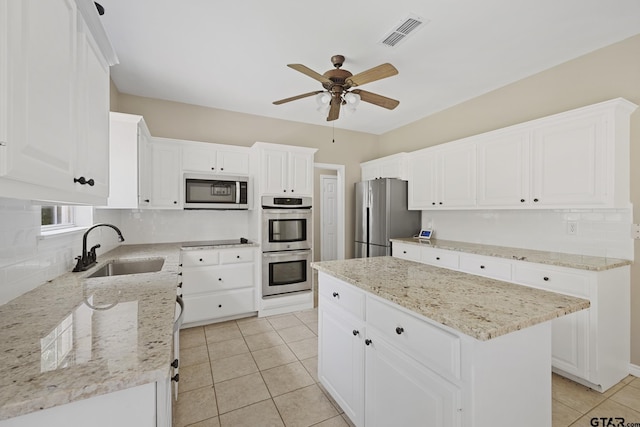 kitchen with sink, a kitchen island, light stone counters, white cabinetry, and stainless steel appliances