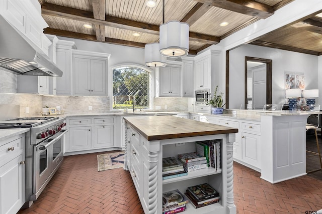 kitchen with stainless steel appliances, butcher block counters, a kitchen island, and wall chimney range hood