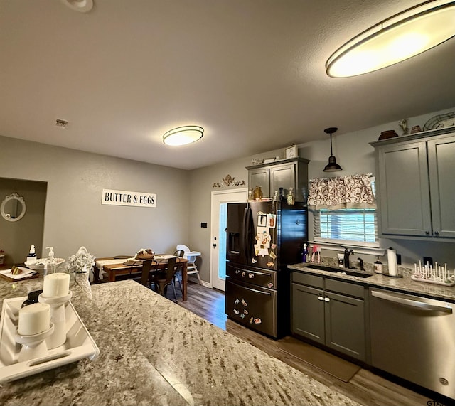 kitchen featuring sink, dark hardwood / wood-style floors, light stone counters, decorative light fixtures, and stainless steel dishwasher