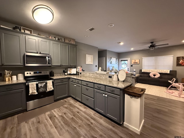 kitchen featuring dark stone countertops, gray cabinetry, dark hardwood / wood-style flooring, kitchen peninsula, and stainless steel appliances