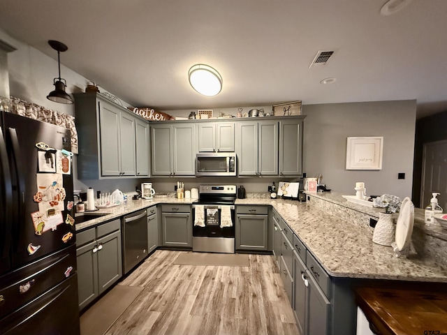 kitchen with appliances with stainless steel finishes, gray cabinetry, light stone counters, light hardwood / wood-style floors, and decorative light fixtures