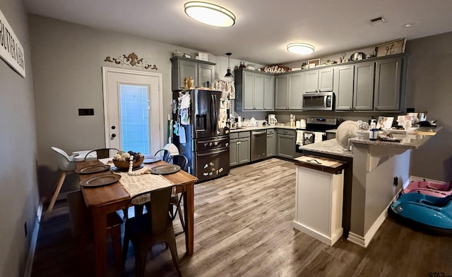 kitchen featuring gray cabinets, appliances with stainless steel finishes, hanging light fixtures, wood-type flooring, and kitchen peninsula