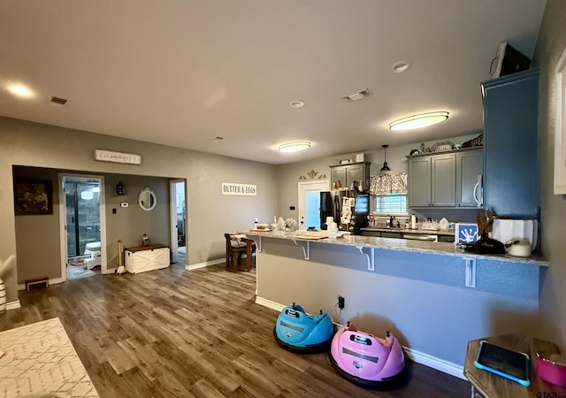 kitchen featuring dark wood-type flooring, a kitchen bar, decorative light fixtures, gray cabinets, and kitchen peninsula