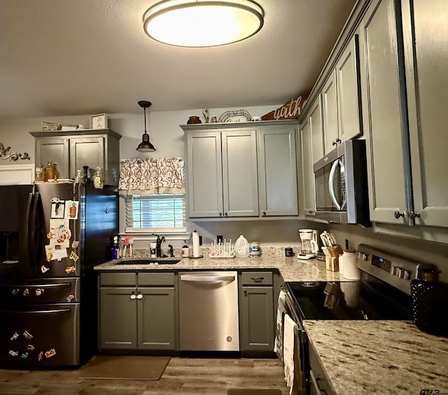 kitchen featuring dark hardwood / wood-style floors, sink, hanging light fixtures, light stone counters, and stainless steel appliances