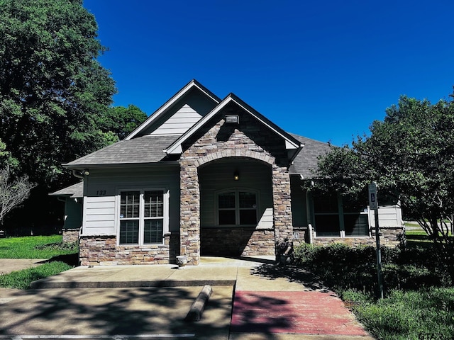 craftsman inspired home featuring stone siding, a shingled roof, and covered porch