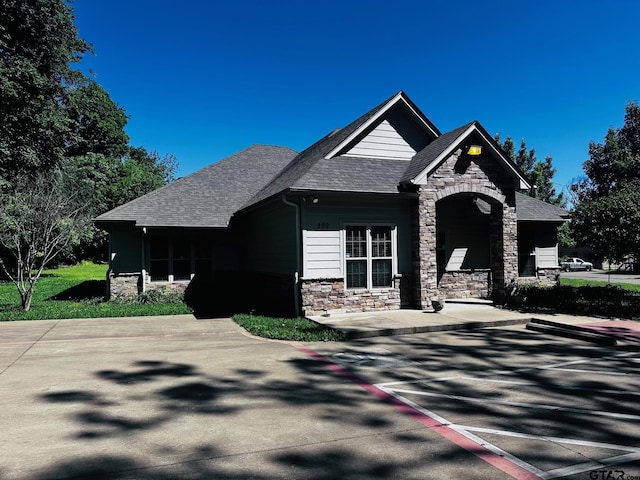 craftsman-style house featuring stone siding, uncovered parking, and a shingled roof