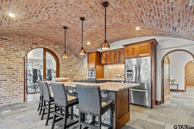 kitchen featuring brick ceiling, a kitchen bar, stainless steel appliances, decorative light fixtures, and vaulted ceiling