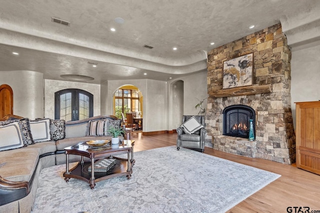 living room with light hardwood / wood-style flooring, french doors, and a stone fireplace