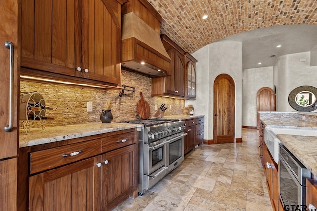 kitchen featuring double oven range, brick ceiling, backsplash, lofted ceiling, and light stone countertops