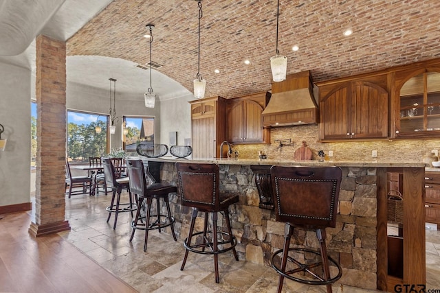 kitchen with brick ceiling, hanging light fixtures, custom range hood, vaulted ceiling, and sink