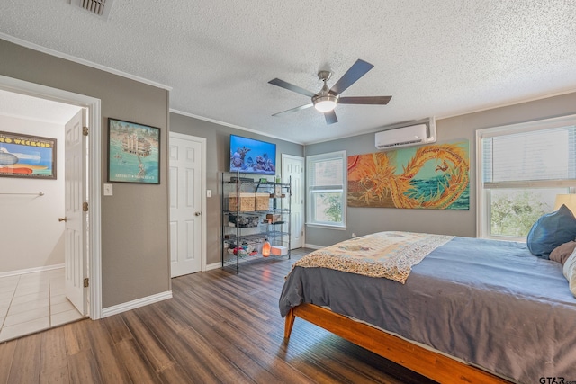 bedroom with crown molding, a wall unit AC, visible vents, wood finished floors, and baseboards