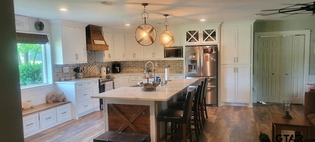 kitchen with custom exhaust hood, appliances with stainless steel finishes, white cabinetry, and wood finished floors