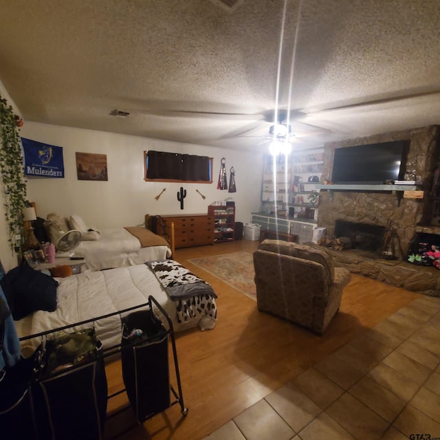 living room with a stone fireplace, wood finished floors, a ceiling fan, and a textured ceiling