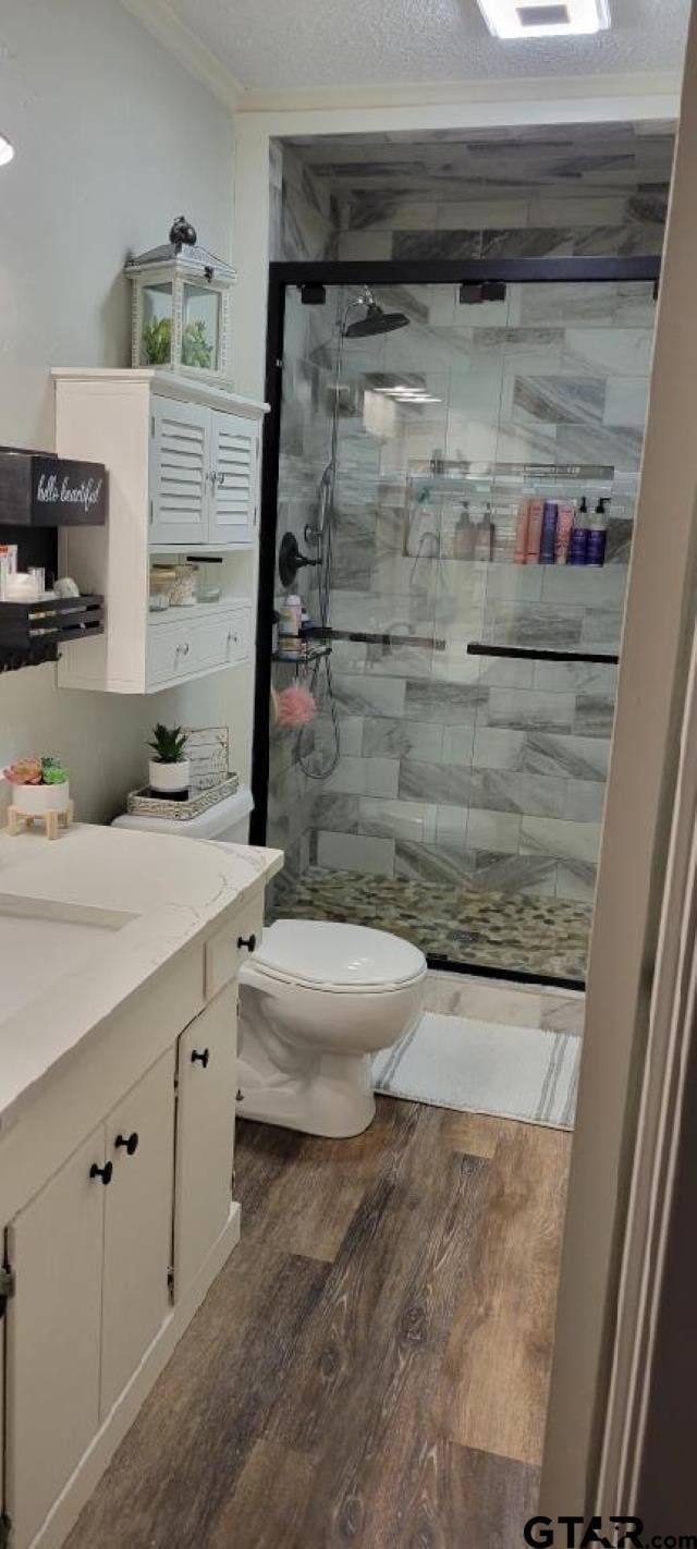 bathroom with toilet, a textured ceiling, wood finished floors, a shower stall, and crown molding