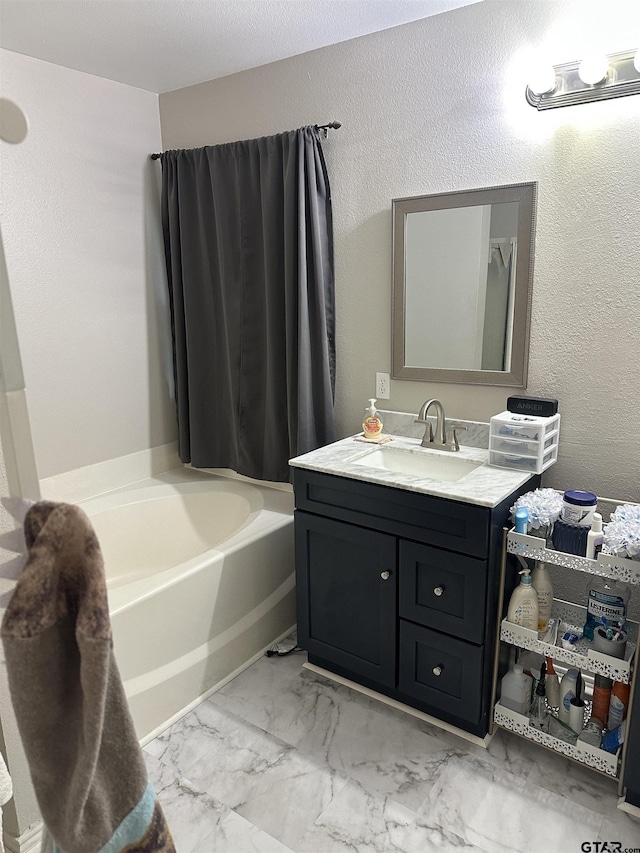 full bathroom with a tub to relax in, marble finish floor, vanity, and a textured wall