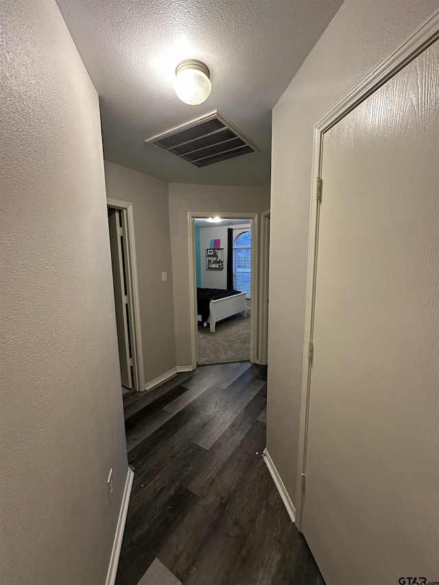 hall featuring visible vents, baseboards, a textured ceiling, and dark wood-style floors